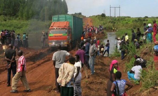 Large truck stuck in mud on Ugandan road. Crowd of people stand nearby.