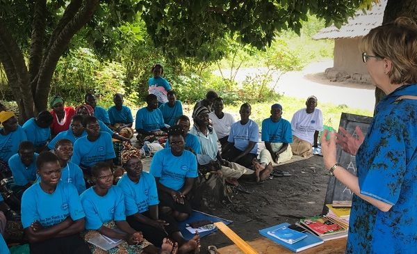 Karon presenting to group of women seated on ground.