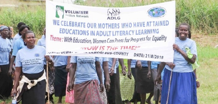 Ugandan women holding sign celebrating literacy learning.