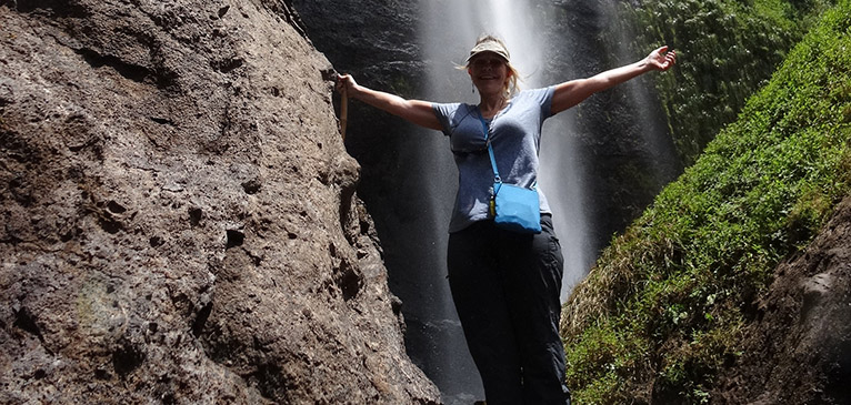 Woman standing in front of waterfall with arms in air.